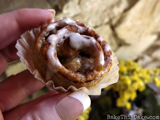Holding Mini Apple Cinnamon Bun with yellow porch flowers by BakeThisCake